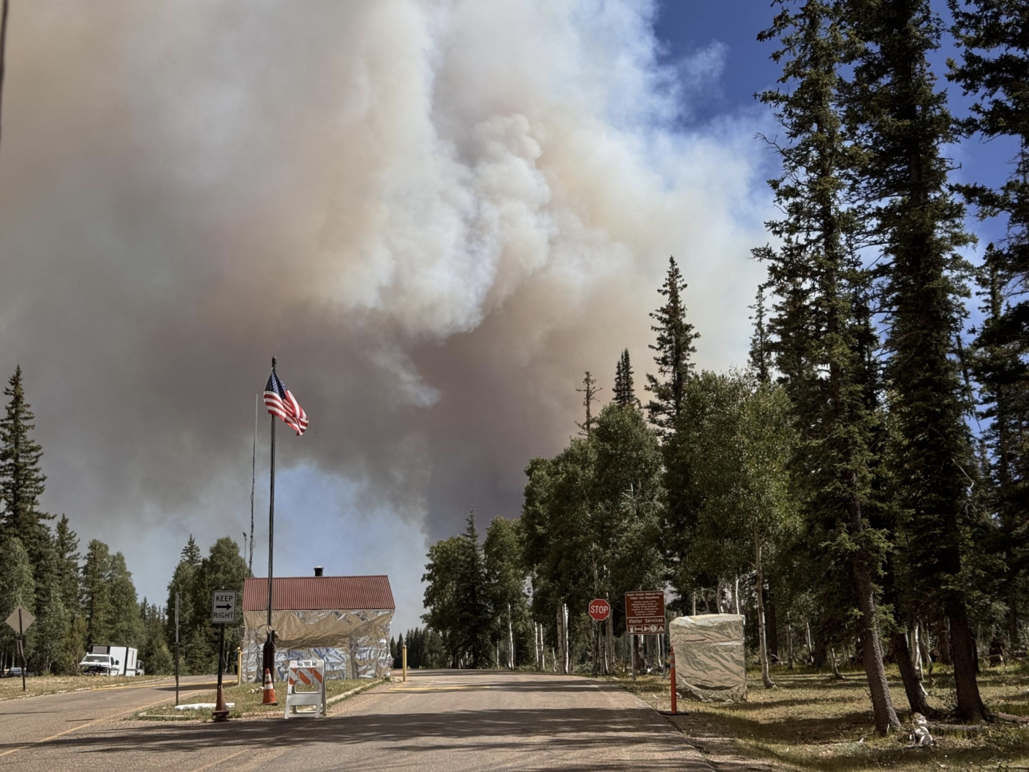 Smoke billows into the sky behind a building wrapped in foil-like fire retardant material.