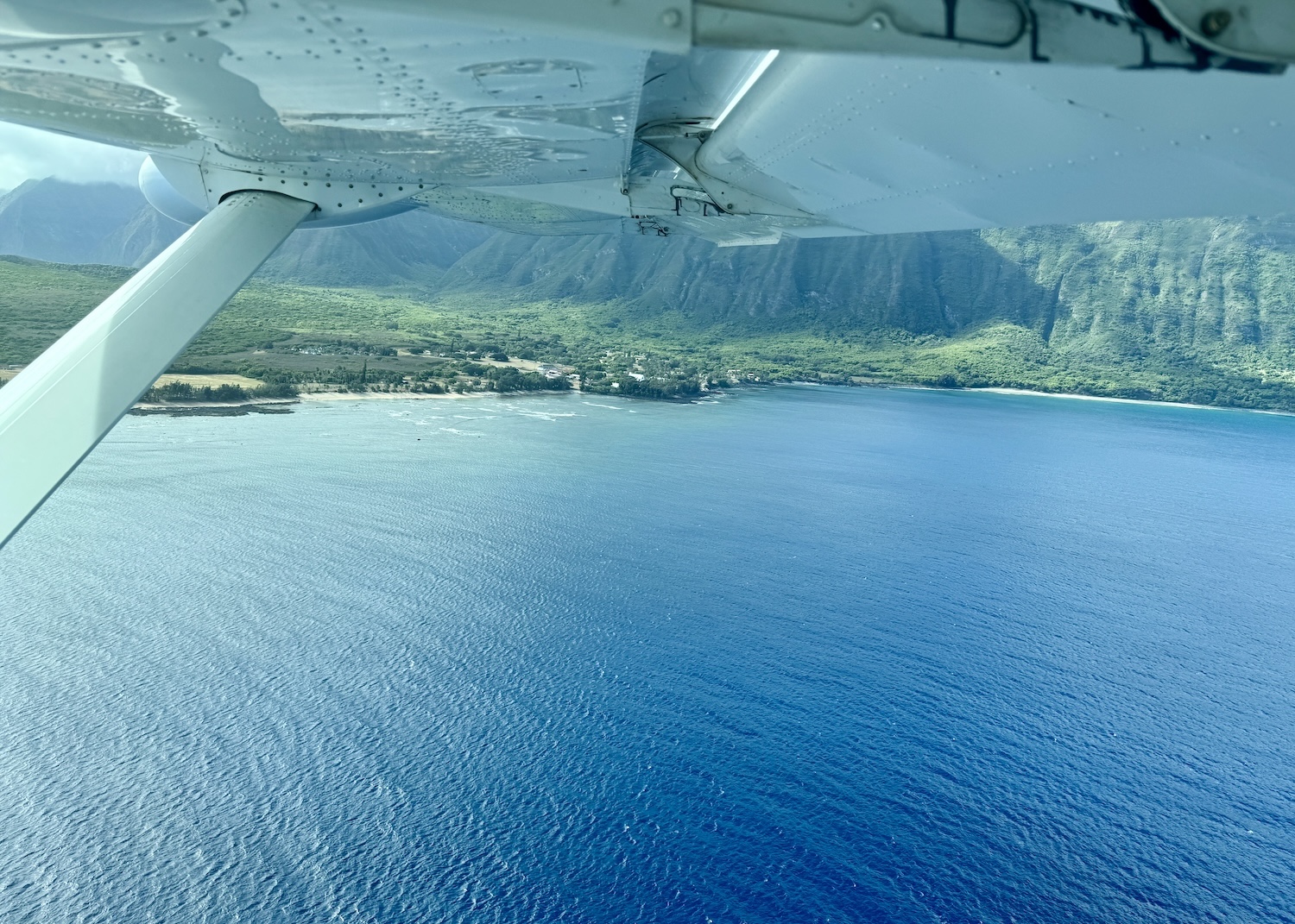 An island is seen surrounded by a water from the window of small plane.