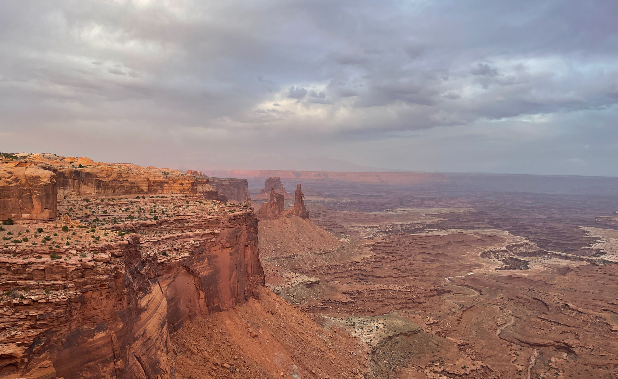 Tall canyon walls with river winding across the bottom of the canyon. The view is a little obscured by a think haze and clouds.