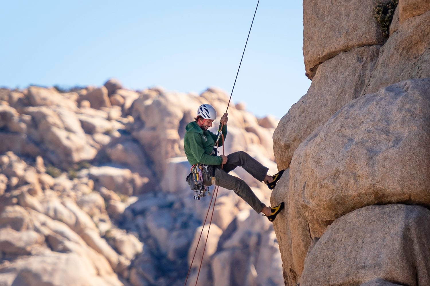 A rock climber rappelling down a rock formation with a rope and harness.