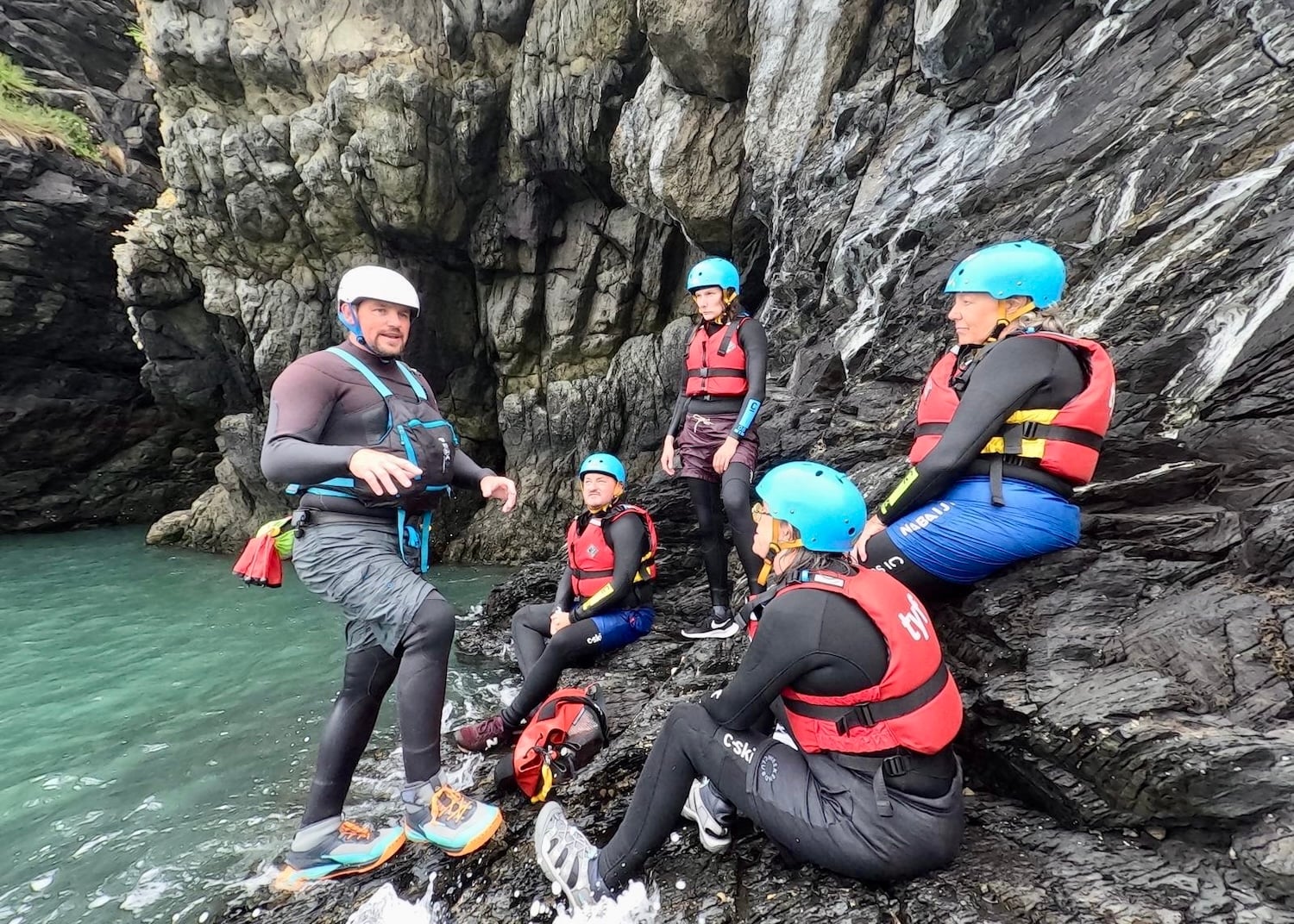The coasteering group chats on rocks.