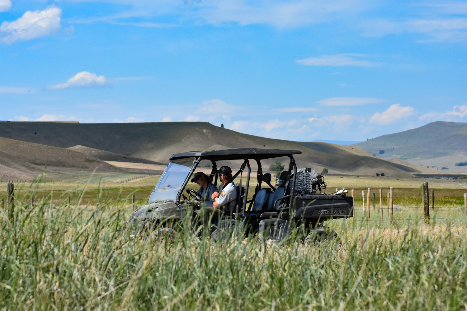 Two people in an ATV drive through a grassy, open prairie at Grant-Kohrs Ranch National Historic Site