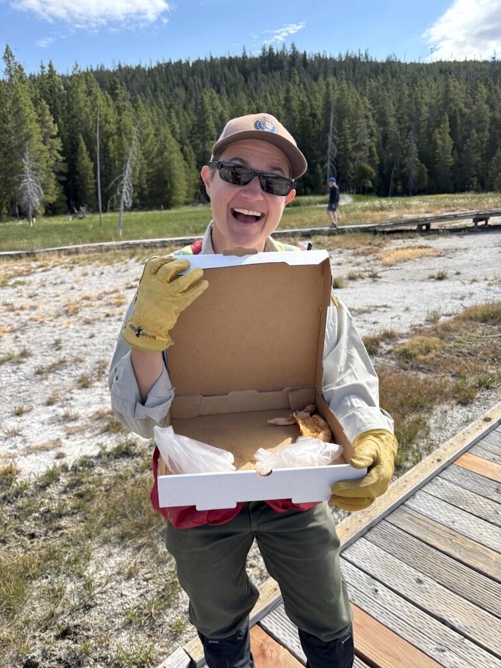 Yellowstone National Park Geology Program volunteer Tara Cross smiles and shows off a pizza box found on Geyser Hill in Upper Ge
