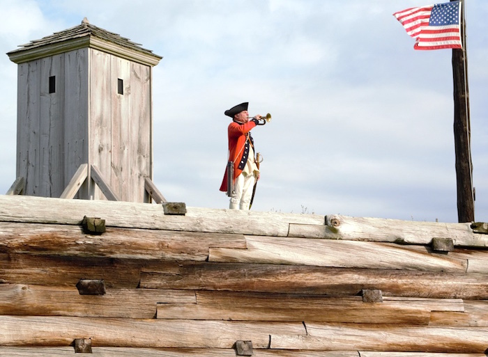 Robert Allers stands at attention on the fort wall playing a bugle/ NPS, Volunteer Robert Allers