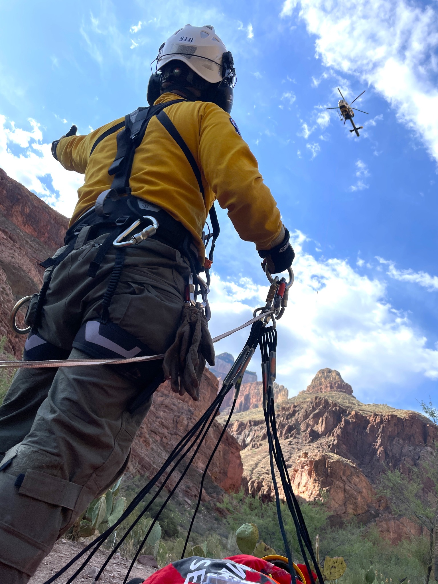 Grand Canyon Rescues A rescuer in a helmet looks up at a helicopter approaching amid the cliffs of the Grand Canyon.