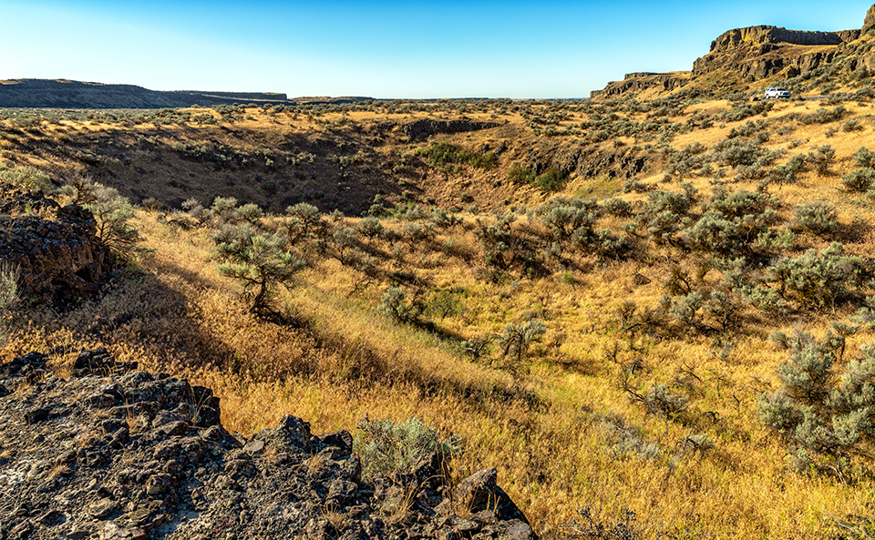 I spy with my little eye a tiny white SUV and one heck of a pothole, Drumheller Channels National Natural Landmark, Ice Age Floods National Geologic Trail / Rebecca Latson I spy with my little eye a tiny white SUV and one heck of a pothole, Drumheller Channels National Natural Landmark, Ice Age Floods National Geologic Trail / Rebecca Latson