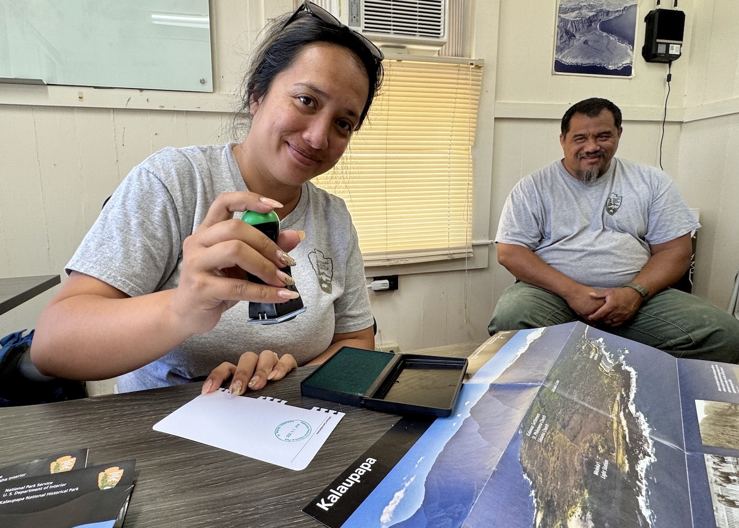 At park headquarters, Jessica Espaniola provides a NPS passport stamp as her husband Albert Espaniola looks on.