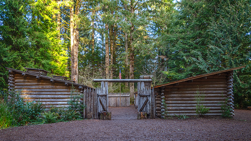A front view of a log fort with an American flag surrounded by tall green trees at Lewis and Clark National Historical Park.