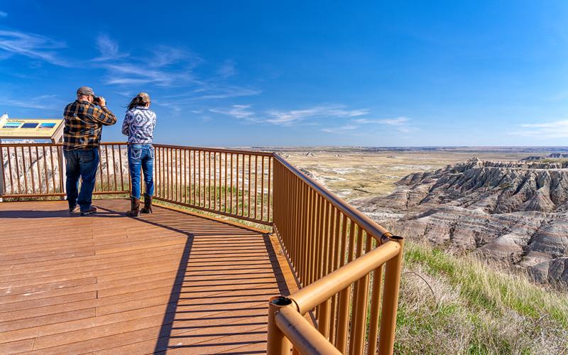 Two people on a viewing platform looking out to the distant formations in Badlands National Park in South Dakota