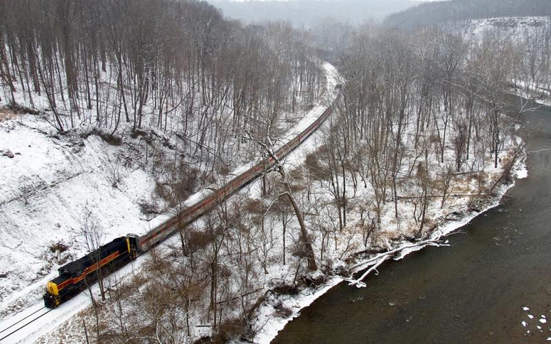 The leading line of a train on train tracks over a snowy landscape with bare trees beneath a white sky, Cuyahoga Valley National Park