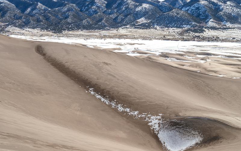 A view from a tall sand dune looking out toward the east, across the snow-covered expanse of flat land where frozen Medano Creek usually flows, Great Sand Dunes National Park and Preserve