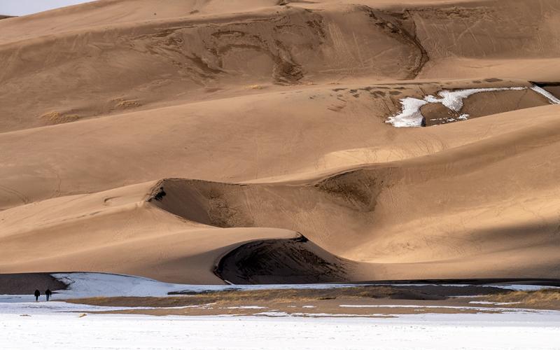 A telephoto view of the sinuous and shadowy sand dunes above a winter ground of snow and ice, Great Sand Dunes National Park and Preserve