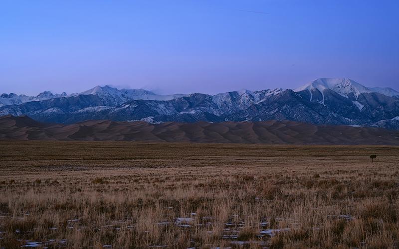 A wide-angle view of valley, sand dunes, and mountains just after sunset, with a blue and purple sky, Great Sand Dunes National Park and Preserve