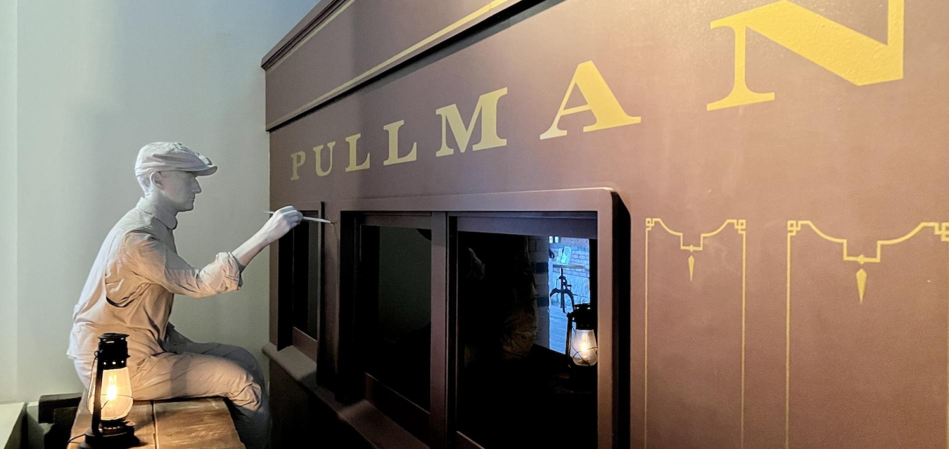 In the Pullman National Historical Park visitor center, a display shows a man hand painting a wooden Pullman railroad car. In the Pullman National Historical Park visitor center, a display shows a man hand painting a wooden Pullman railroad car.