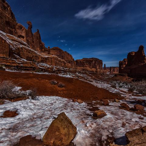 Winter ice and red rock of Park Avenue at midnight in Arches National Park in Utah