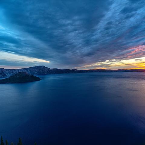 A sunburst sunrise climbing above the caldera rim and beginning to shine on Wizard Island in Crater Lake National Park
