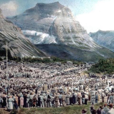 An old colorized postcard photo of the crowds at Logan Pass for the dedication of Going-to-the-Sun Road in Glacier National Park