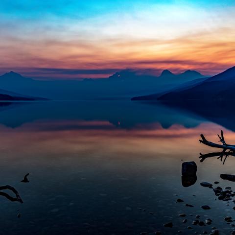 A smoky sunrise over Lake McDonald in Glacier National Park, Montana, caused by the Sprague Fire, which can be seen on the mountain in the background