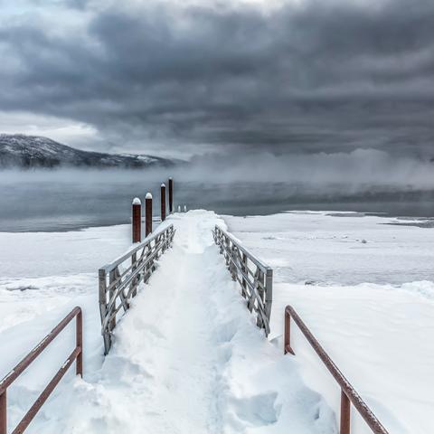 A gray and white, almost monochromatic, morning with dark, steel-gray clouds hiding the mountains from view at Lake McDonald, Glacier National Park