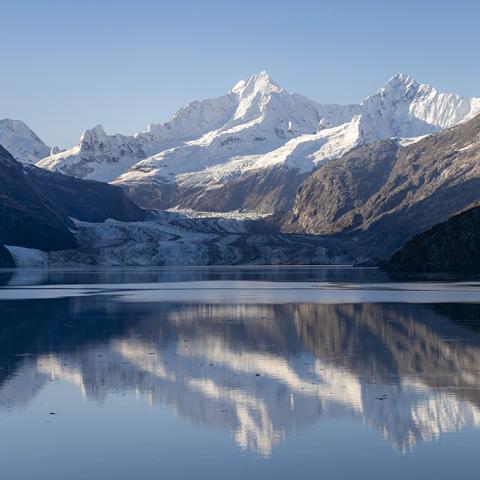 A body of water reflecting snow-capped rugged mountains and a glacier in Johns Hopkins Inlet at Glacier Bay National Park and Preserve