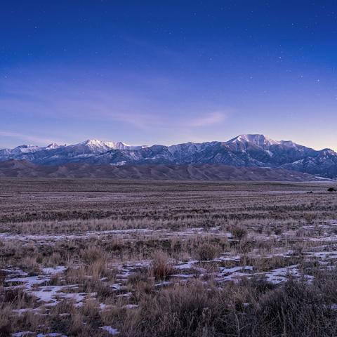 The winter night sky with a few remaining stars as the landscape begins to brighten with the coming sunrise over mountains and giant sand dunes at Great Sand Dunes National Park and Preserve.