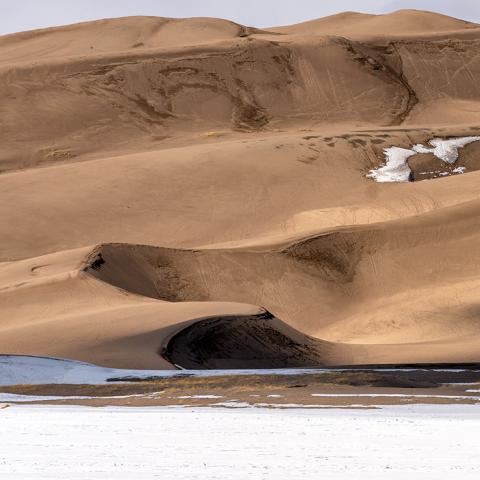 A telephoto view of the sinuous and shadowy sand dunes above a winter ground of snow and ice, Great Sand Dunes National Park and Preserve