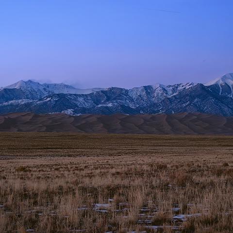 A wide-angle view of valley, sand dunes, and mountains just after sunset, with a blue and purple sky, Great Sand Dunes National Park and Preserve