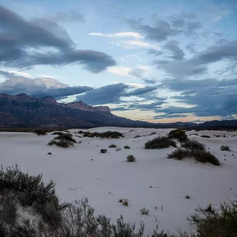 A cloudy, pre-sunrise view of white sand dunes with mountains in the background, Guadalupe Mountains National Park
