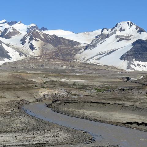 A brown glacier flowing between two snowy mountains and emptying out into a brown river in Valley of Ten Thousand Smokes, Katmai National Park and Preserve