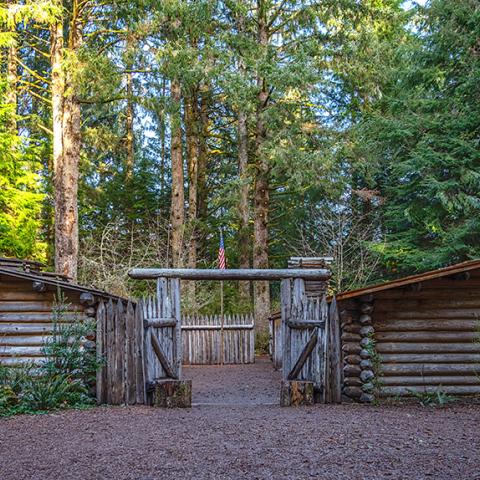 A front view of a log fort with an American flag surrounded by tall green trees at Lewis and Clark National Historical Park.