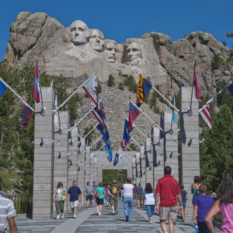 Visitors walking along the Avenue of Flags with Mount Rushmore in the background.