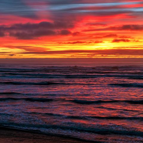 Layers of colorful clouds colored orange and gold by the setting sun over the Pacific Ocean and Kalaloch Beach, Olympic National Park