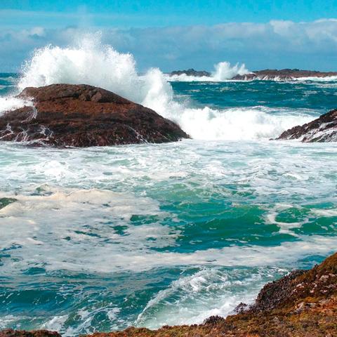 The teal-blue sea and waves crashing over large rocks at Pacific Rim National Park Reserve