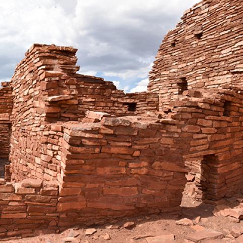 A red sandstone pueblo with one large wall and the remains of several rooms at Wupatki National Monument.