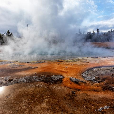 A heavily-steaming Emerald Pool surrounded by orange bacterial mats at Black Sand Basin in Yellowstone National Park