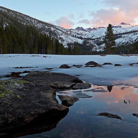 Sunset alpenglow on the mountains above reflections on a frozen lake in Upper Lyell Canyon, Yosemite National Park