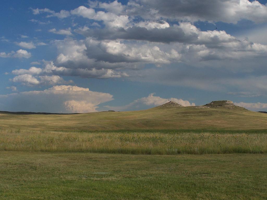 The Agate Fossil Hills covered in green grass with thunderhead in the background at Agate Fossil Beds National Monument.