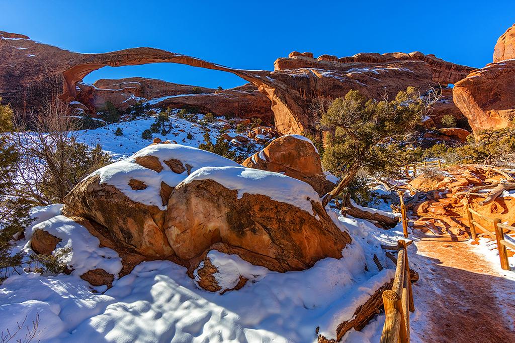 Snow and red rock around Landscape Arch with a frozen sand trail toward the arch in Arches National Park