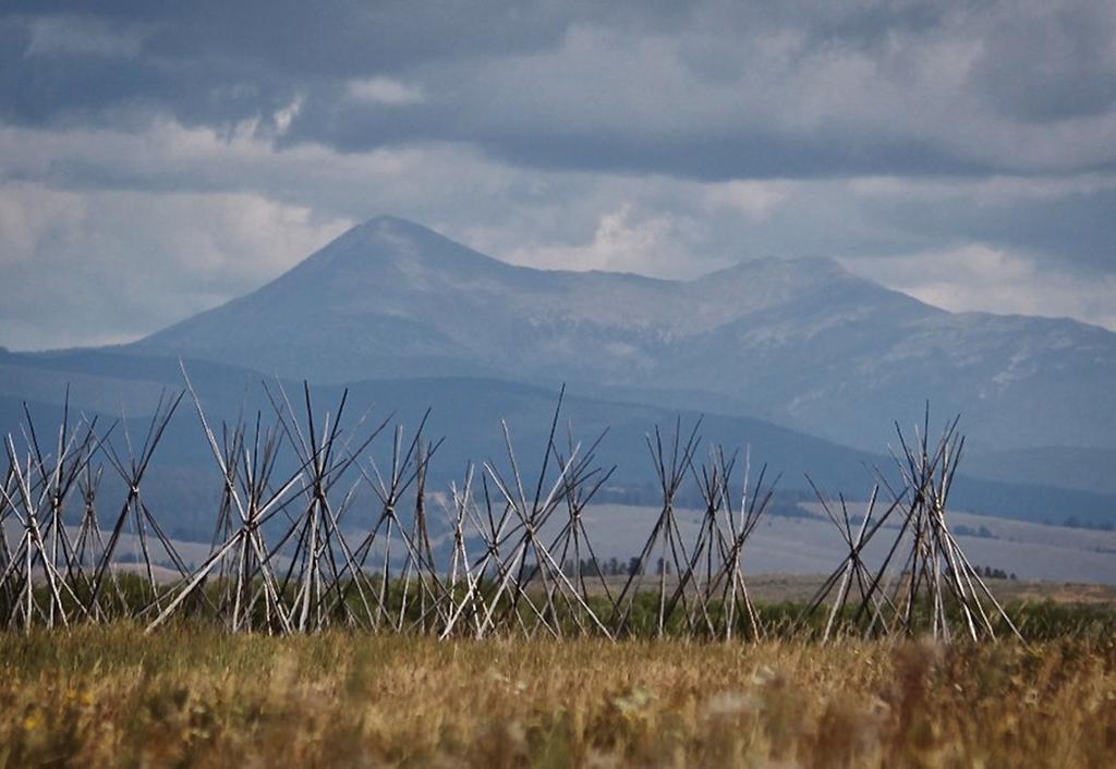 Tipi poles on a dry grass prairie with tall blue mountains in the distance and dramatic storm clouds overhead, Big Hole National Battlefield