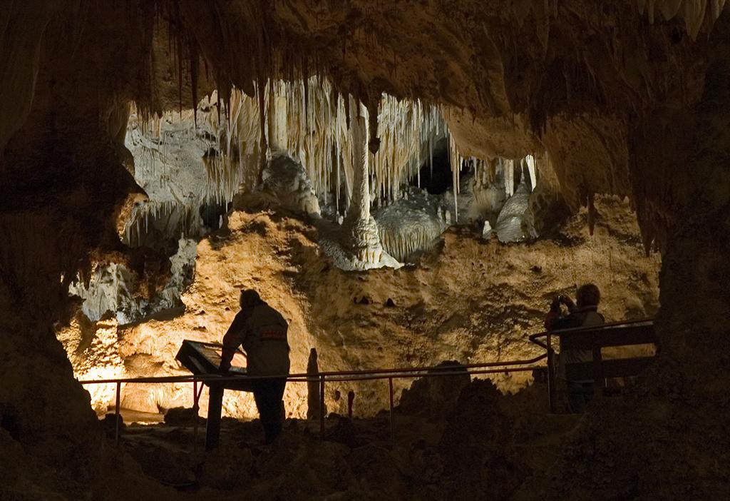 Silhouetted people looking at and photographing a small alcove of stalagtites and stalagmites in Carlsbad Caverns National Park