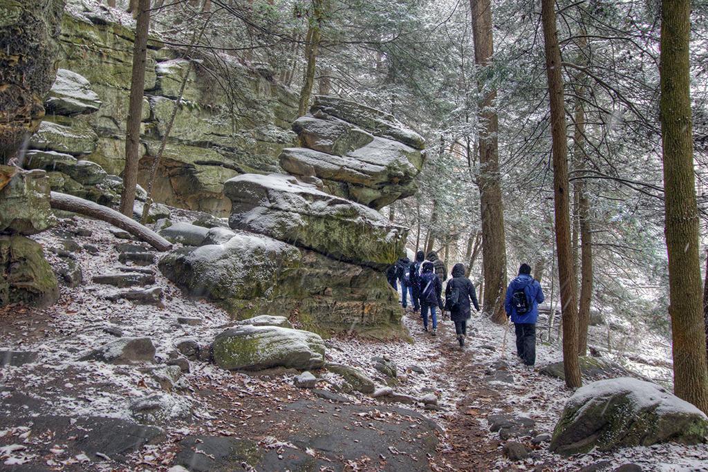Hikers on a snow-dusted trail surrounded by trees and boulders, Cuyahoga Valley National Park