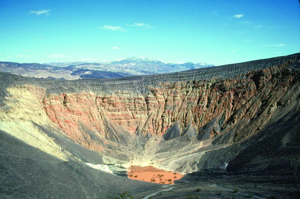 A large crater of red and black rock under a blue sky at Death Valley National Park