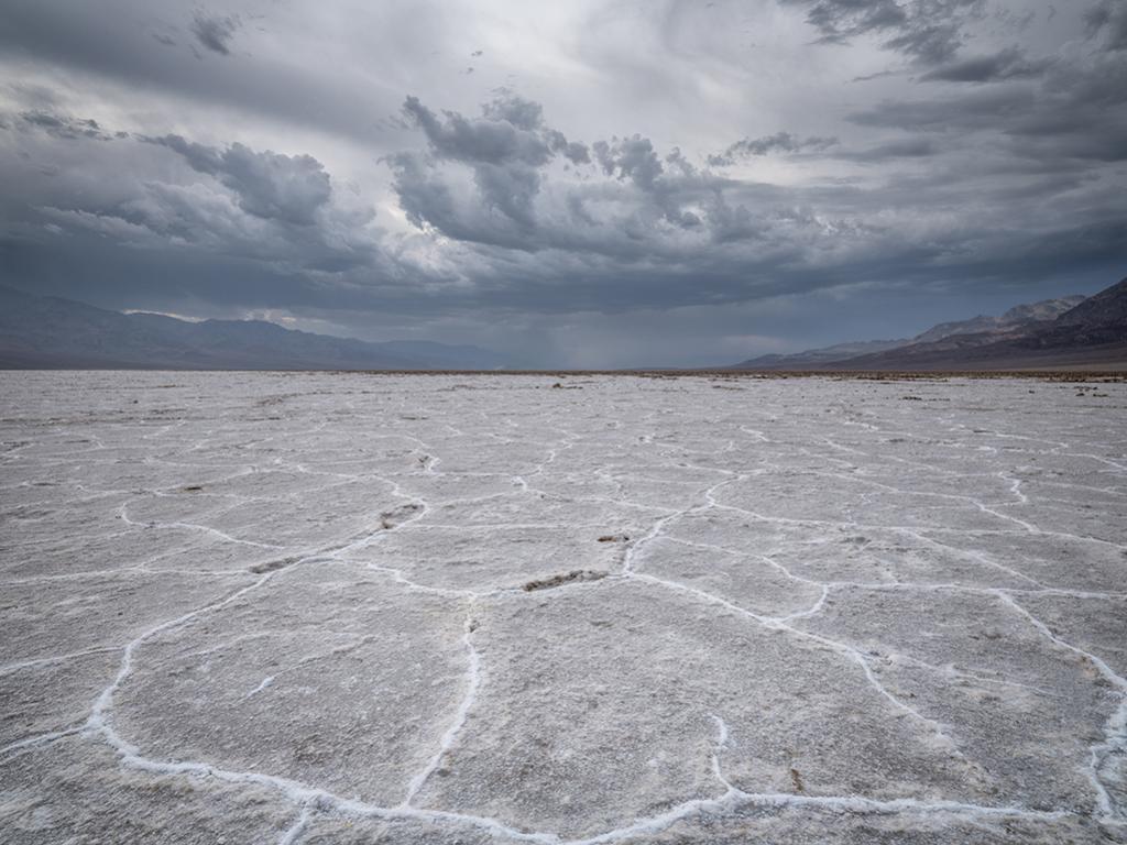 Dark, fluffy storm clouds hovering over the Panamint Mountains and the salt flat at Badwater Basin, Death Valley National Park
