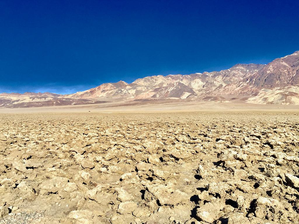 A dry, wrinkled, uneven surface with dry mountains in the background and clear blue sky overhead at Devil's Golf Course in Death Valley National Park