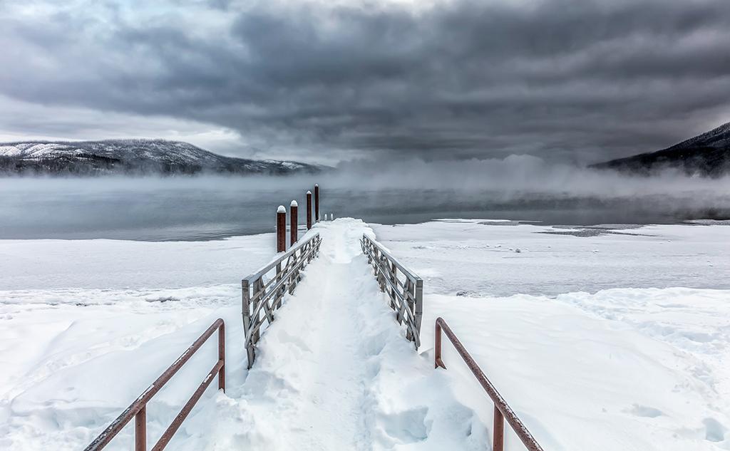 A gray and white, almost monochromatic, morning with dark, steel-gray clouds hiding the mountains from view at Lake McDonald, Glacier National Park