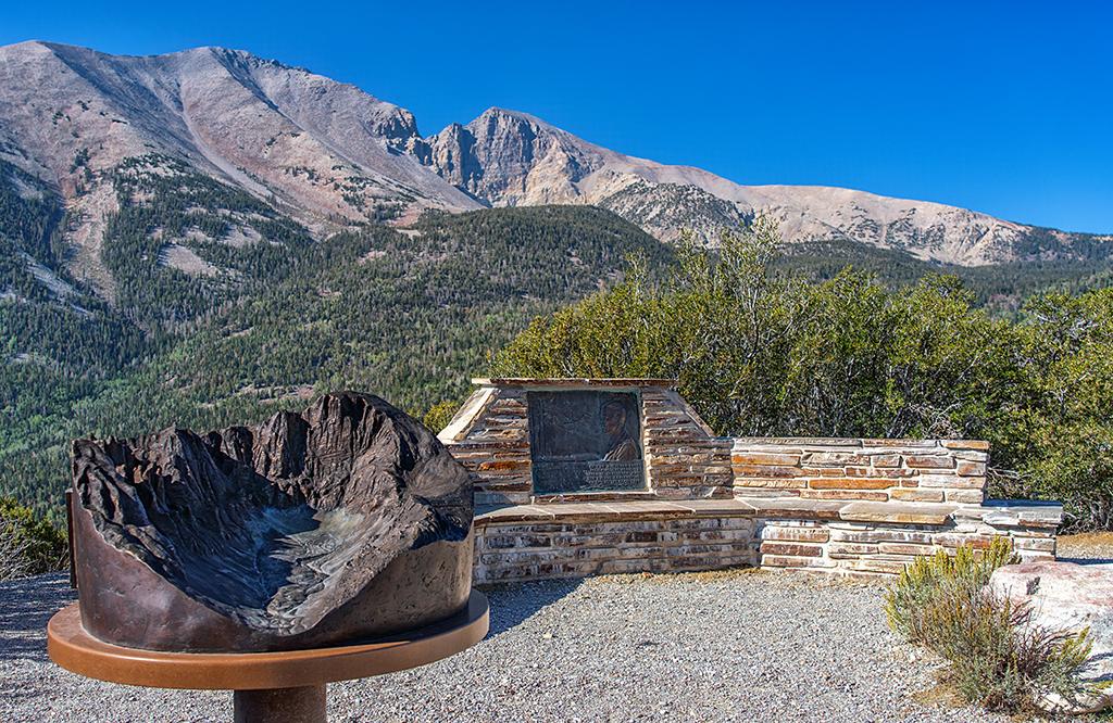 A bronze relief map of Wheeler Cirque and a commemorative plaque and stone seat with Doso Doyabi and Wheeler Peak in the background at Mather Overlook, Great Basin National Park