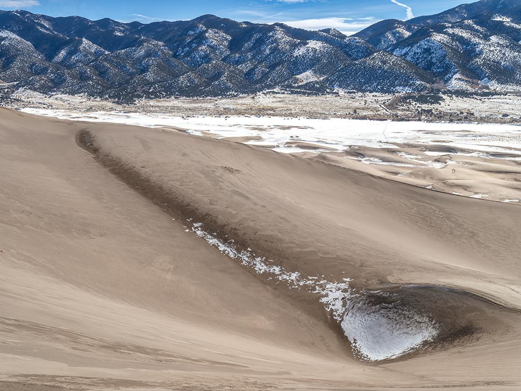 A view from a tall sand dune looking out toward the east, across the snow-covered expanse of flat land where frozen Medano Creek usually flows, Great Sand Dunes National Park and Preserve