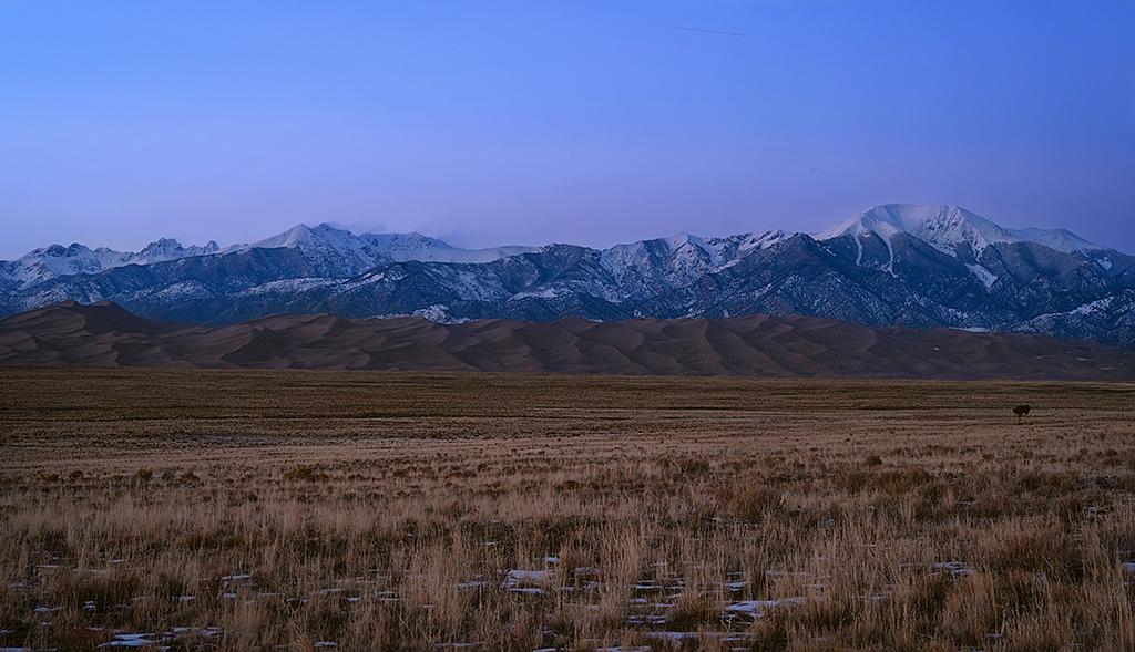 A wide-angle view of valley, sand dunes, and mountains just after sunset, with a blue and purple sky, Great Sand Dunes National Park and Preserve