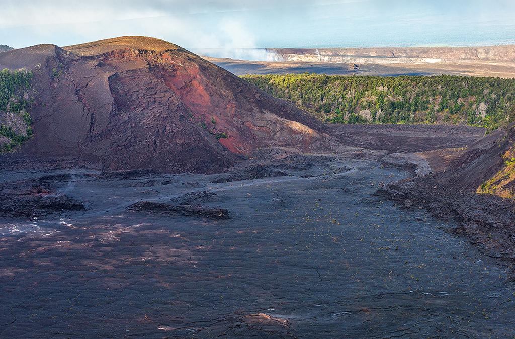 A wide-angle morning view looking down on the flat, solifidied lava lake of the Kilauea Iki Trail, with the Pu‘u Pua‘i cinder cone in the background and a smoking Halemaumau Crater in the distance in Hawai'i Volcanoes National Park