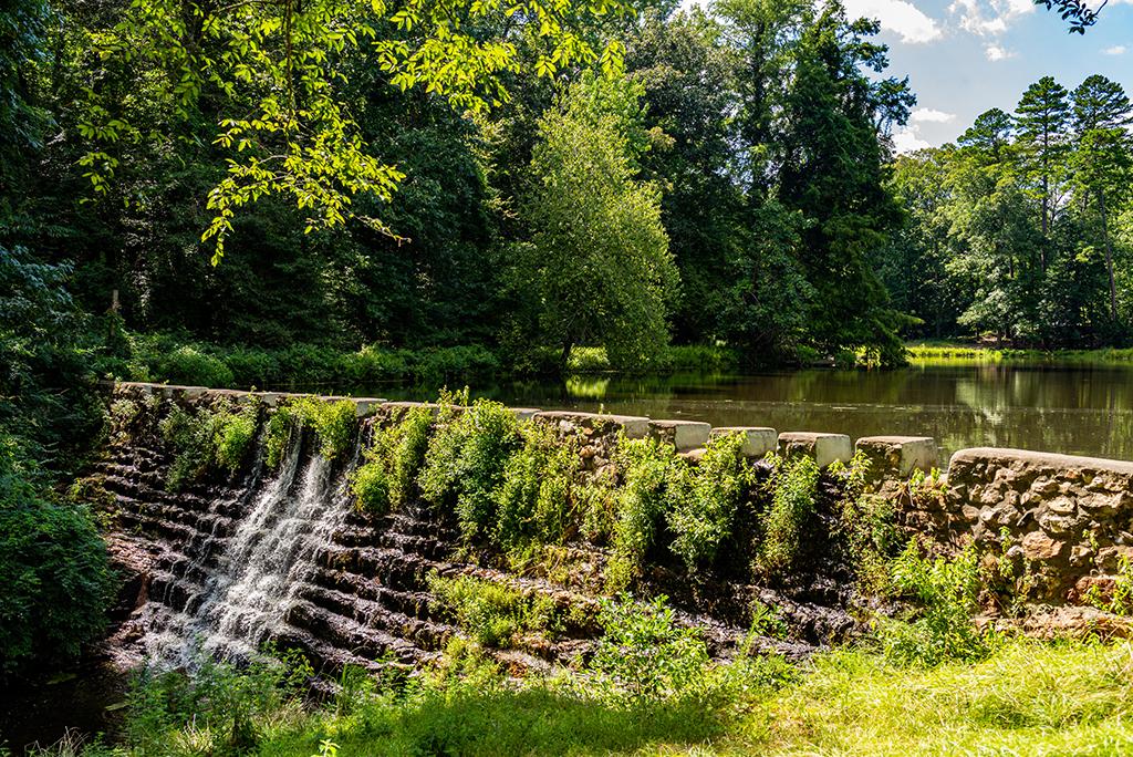 Water flows over a terraced dam and lush vegetation surround the pond on a sunny day in Hot Springs National Park